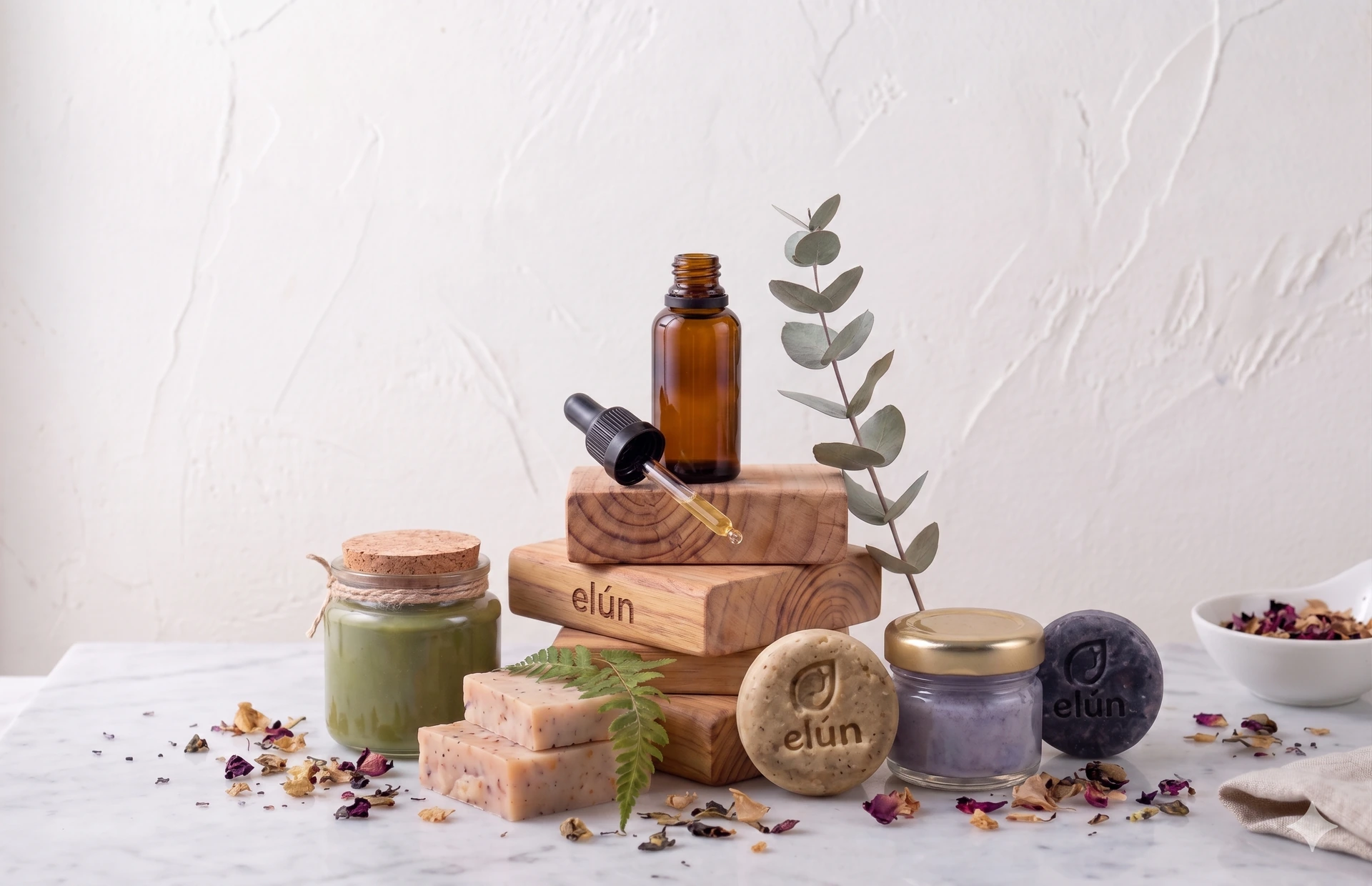 Bodegón de la línea Elún: shampoo sólido, aceite, mascarilla y jabones sobre bloques de madera con eucalipto